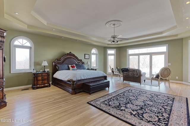 bedroom with multiple windows, a raised ceiling, light wood-style flooring, and baseboards