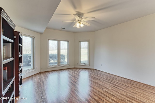 empty room featuring ceiling fan, wood finished floors, visible vents, and baseboards