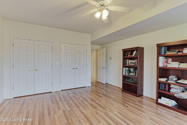 bedroom with light wood-type flooring, ceiling fan, baseboards, and two closets