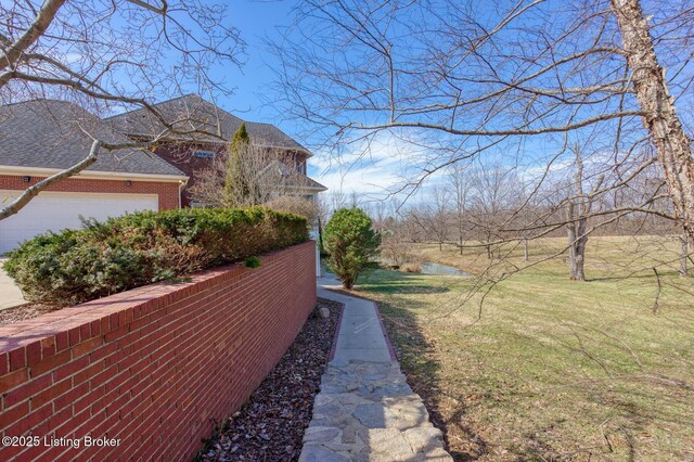 view of side of home with a garage, brick siding, a yard, and a shingled roof