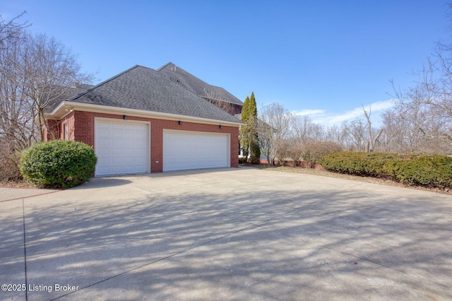 view of home's exterior with an attached garage, a shingled roof, concrete driveway, and brick siding