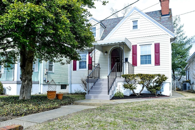 view of front of house featuring a shingled roof, a front yard, a chimney, and central air condition unit