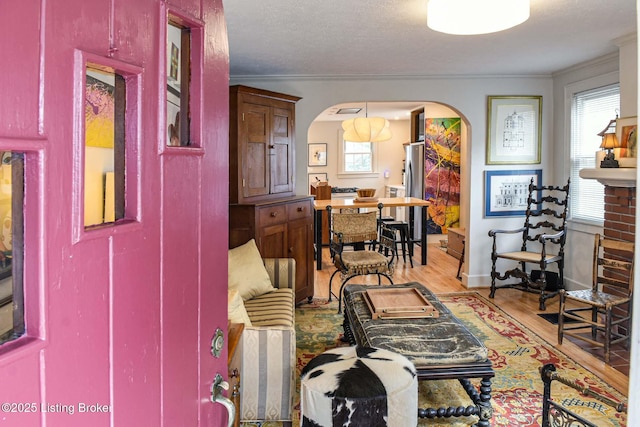 interior space featuring arched walkways, a textured ceiling, baseboards, light wood-style floors, and ornamental molding