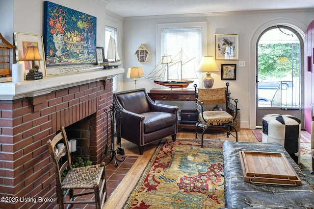 living area with a brick fireplace, crown molding, and wood finished floors