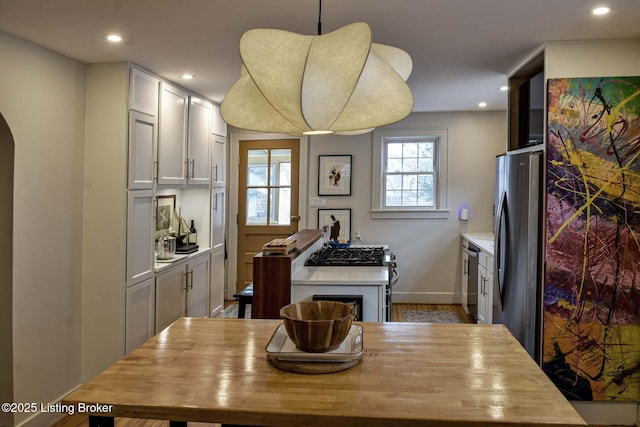 kitchen with arched walkways, white cabinets, light countertops, appliances with stainless steel finishes, and hanging light fixtures