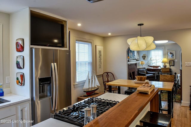 kitchen featuring arched walkways, hanging light fixtures, stainless steel refrigerator with ice dispenser, a wealth of natural light, and gas range oven