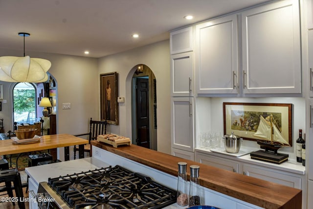 kitchen with arched walkways, recessed lighting, butcher block counters, white cabinets, and decorative light fixtures