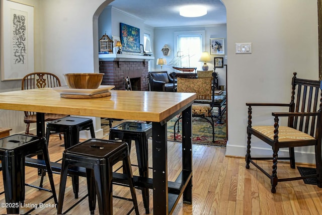 dining space featuring arched walkways, crown molding, light wood-style floors, a brick fireplace, and baseboards