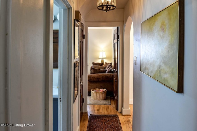 corridor featuring light wood-style floors, arched walkways, and an inviting chandelier