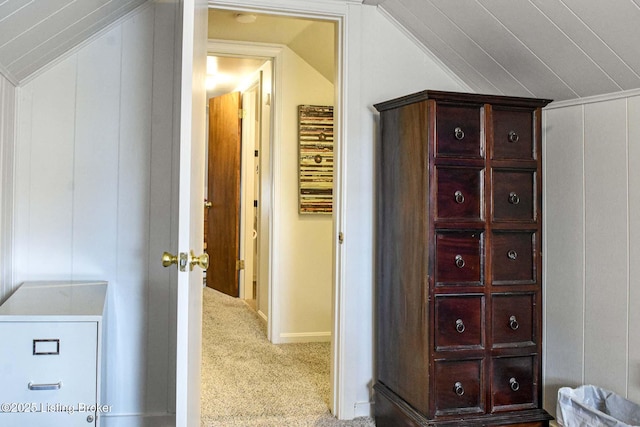 hallway featuring a decorative wall, vaulted ceiling, and light colored carpet