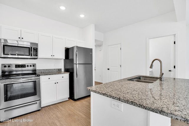 kitchen with light stone counters, light wood finished floors, stainless steel appliances, white cabinets, and a sink