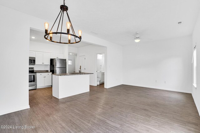 kitchen with dark countertops, appliances with stainless steel finishes, a center island, hanging light fixtures, and white cabinetry