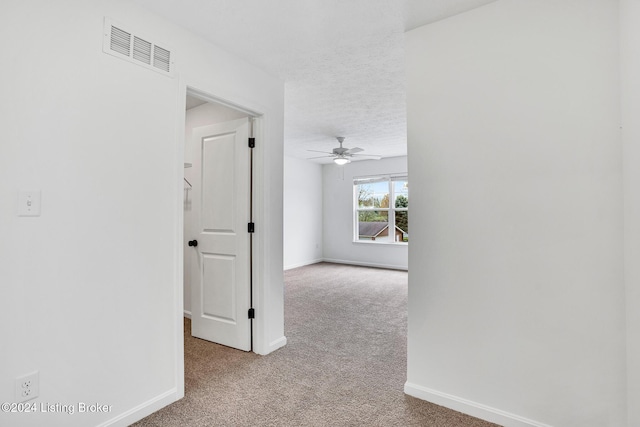 hallway with light colored carpet, visible vents, a textured ceiling, and baseboards