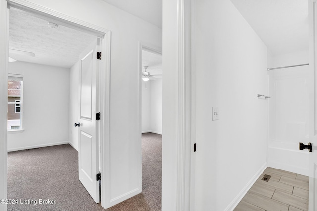hallway featuring baseboards, a textured ceiling, and light colored carpet