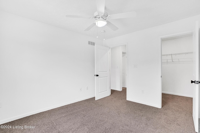unfurnished bedroom with dark carpet, a walk in closet, visible vents, and baseboards