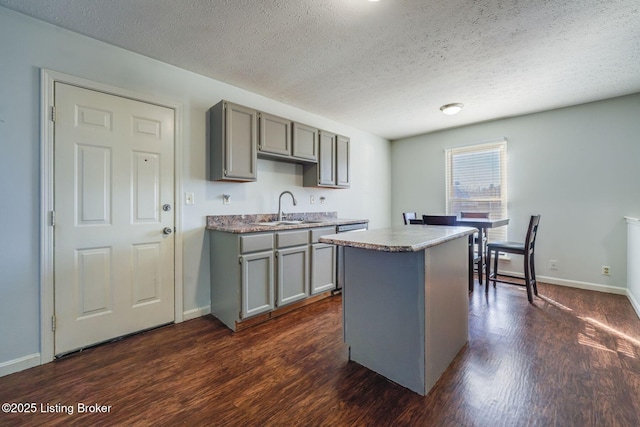 kitchen featuring dark wood-style floors, a sink, a center island, and gray cabinetry