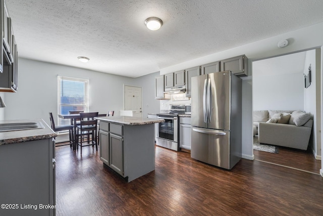 kitchen featuring under cabinet range hood, stainless steel appliances, a kitchen island, gray cabinets, and dark wood-style floors