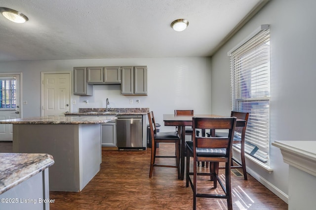 kitchen with dark wood-style flooring, gray cabinetry, a kitchen island, and stainless steel dishwasher