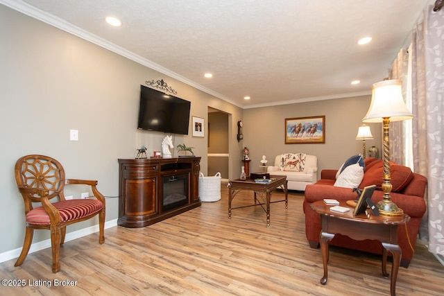 living area with ornamental molding, a glass covered fireplace, light wood-style flooring, and baseboards