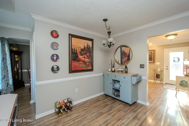 interior space with light wood-style flooring, crown molding, baseboards, and a notable chandelier