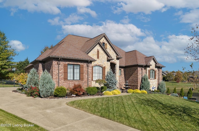 french country home with stone siding, a shingled roof, a front lawn, and brick siding