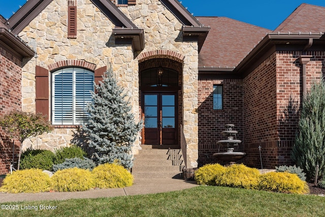 doorway to property with stone siding, french doors, brick siding, and roof with shingles