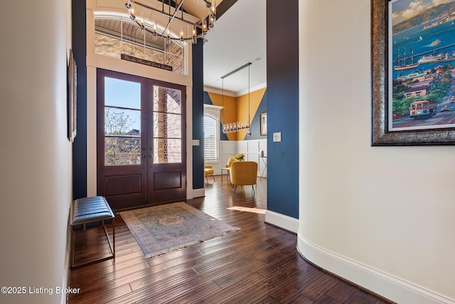 foyer with baseboards, ornamental molding, french doors, dark wood finished floors, and an inviting chandelier