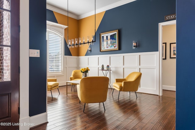 living area with ornamental molding, a decorative wall, wood finished floors, and wainscoting