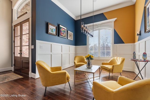 sitting room with dark wood-type flooring, wainscoting, crown molding, and a decorative wall