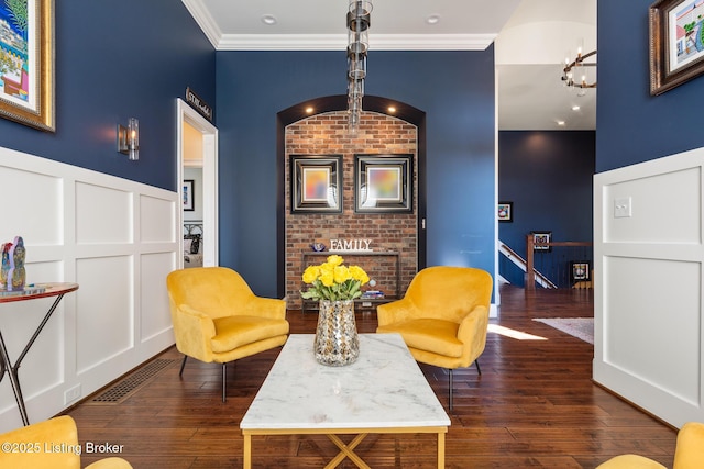 living area featuring visible vents, ornamental molding, a decorative wall, and dark wood-type flooring