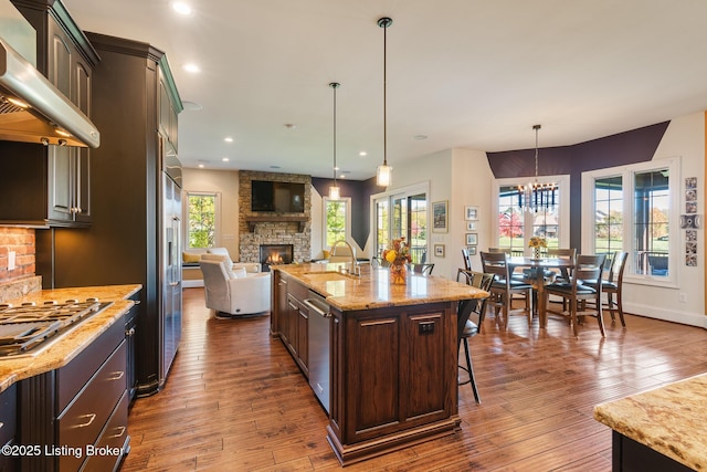 kitchen featuring dark wood-style flooring, open floor plan, dark brown cabinets, an island with sink, and extractor fan