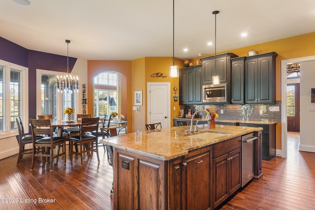 kitchen featuring an island with sink, stainless steel microwave, a sink, and decorative light fixtures