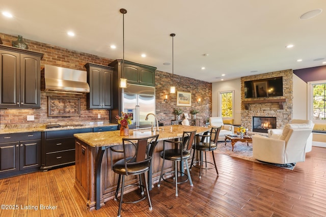 kitchen with open floor plan, wall chimney range hood, appliances with stainless steel finishes, a large island, and pendant lighting