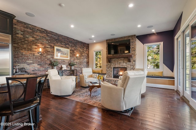 living room featuring dark wood-type flooring, recessed lighting, a stone fireplace, and brick wall