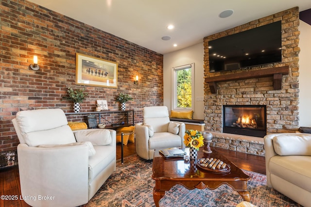 living room featuring dark wood-style flooring, a stone fireplace, and brick wall