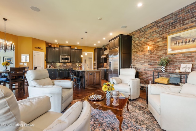 living room featuring recessed lighting, dark wood-style flooring, a notable chandelier, and brick wall