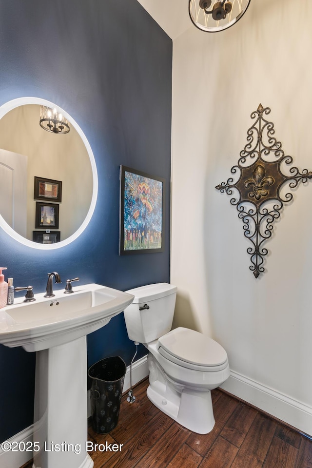 half bath featuring toilet, a sink, wood finished floors, a chandelier, and baseboards