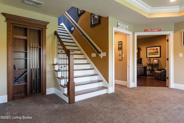 stairway featuring carpet flooring, visible vents, baseboards, ornamental molding, and a raised ceiling