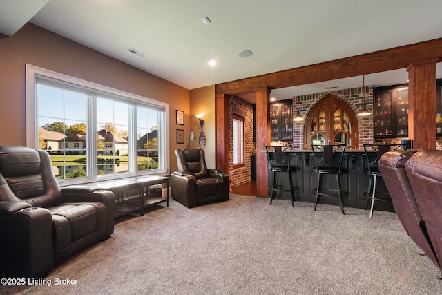 carpeted living area featuring wet bar, visible vents, and brick wall