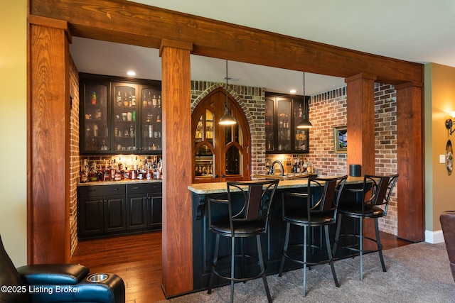 bar featuring dark wood-style floors, brick wall, and wet bar