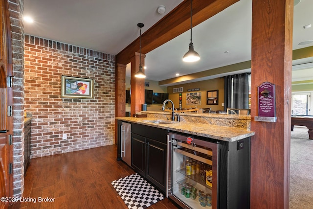 kitchen with beverage cooler, brick wall, light stone counters, pendant lighting, and a sink