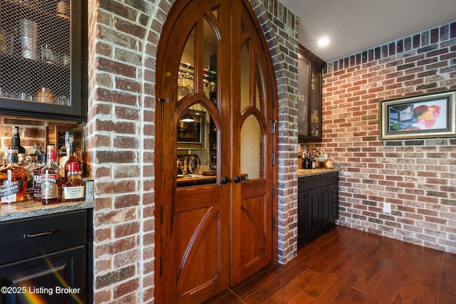 wine area featuring arched walkways, brick wall, dark wood-type flooring, and a dry bar