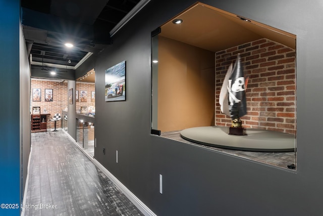 hallway featuring brick wall, wood finished floors, and baseboards