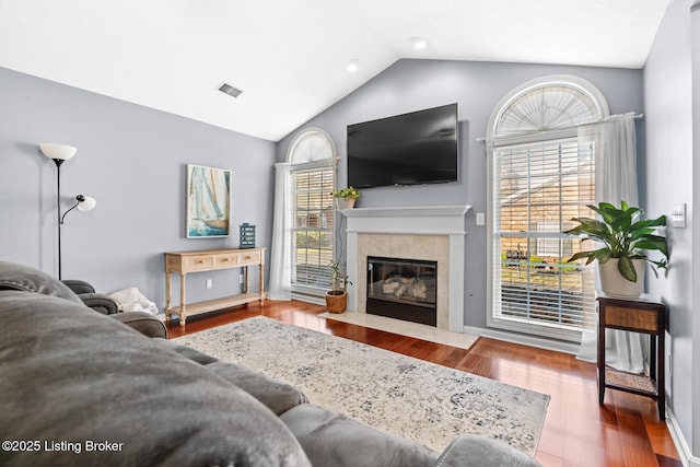 living area with visible vents, a tile fireplace, wood finished floors, baseboards, and vaulted ceiling