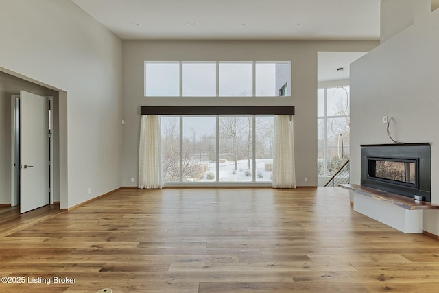 unfurnished living room with a high ceiling, baseboards, a fireplace with raised hearth, and wood finished floors