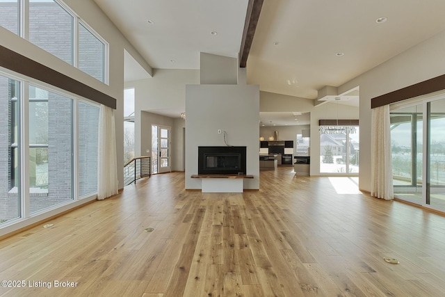 unfurnished living room with a high ceiling, beamed ceiling, light wood-type flooring, and a glass covered fireplace