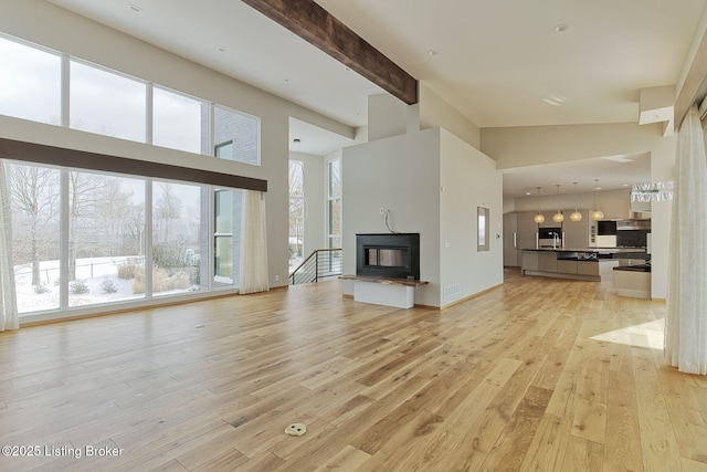 unfurnished living room with a glass covered fireplace, beamed ceiling, light wood-style flooring, and a towering ceiling