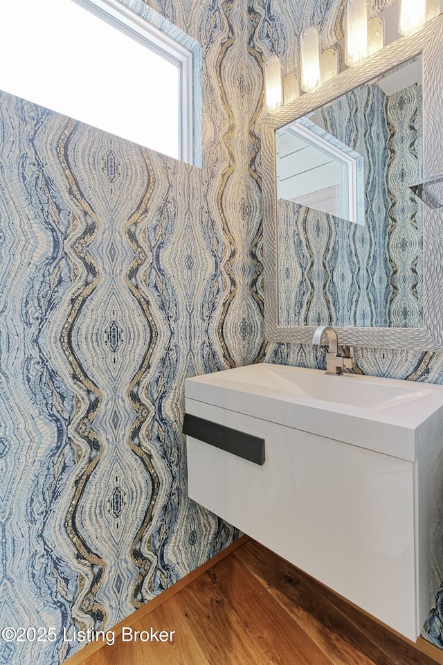 bathroom featuring a sink, wallpapered walls, and wood finished floors