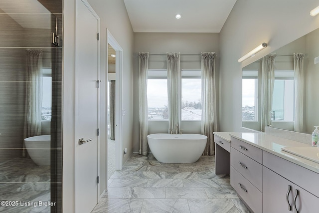 full bath featuring a wealth of natural light, marble finish floor, a freestanding bath, and vanity