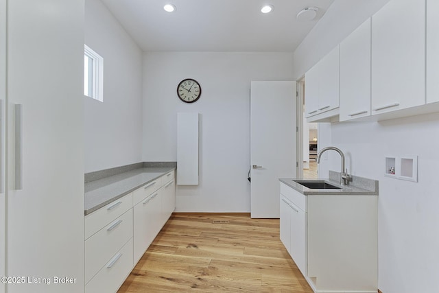 kitchen with light countertops, light wood-type flooring, white cabinetry, a sink, and recessed lighting